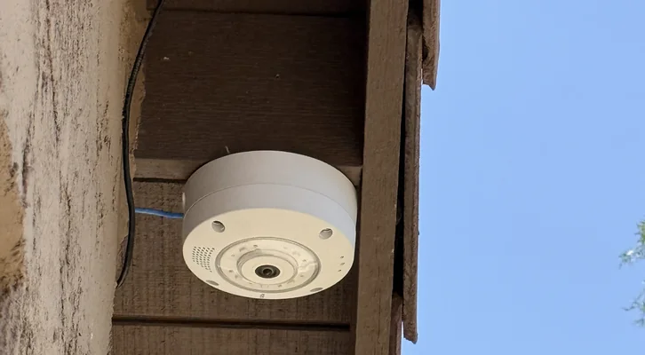 A MOBOTIX Q71 fisheye camera mounted under a timber beam against open sky, network cable run to it