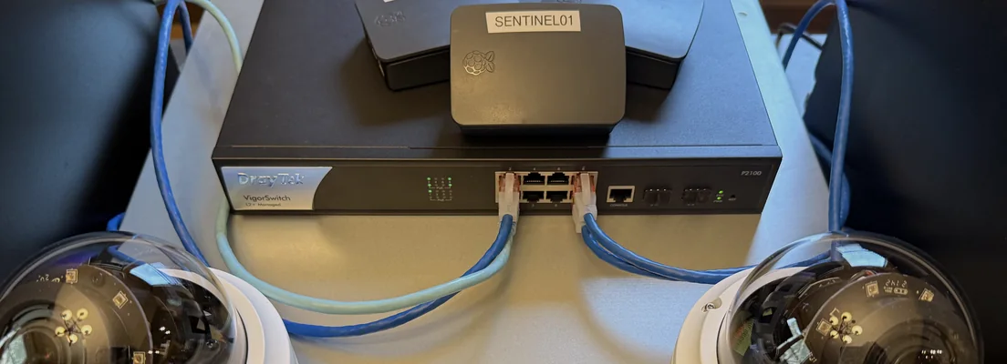A SENTINEL01 unit sitting on a PoE switch, patched network cables running out to two dome cameras